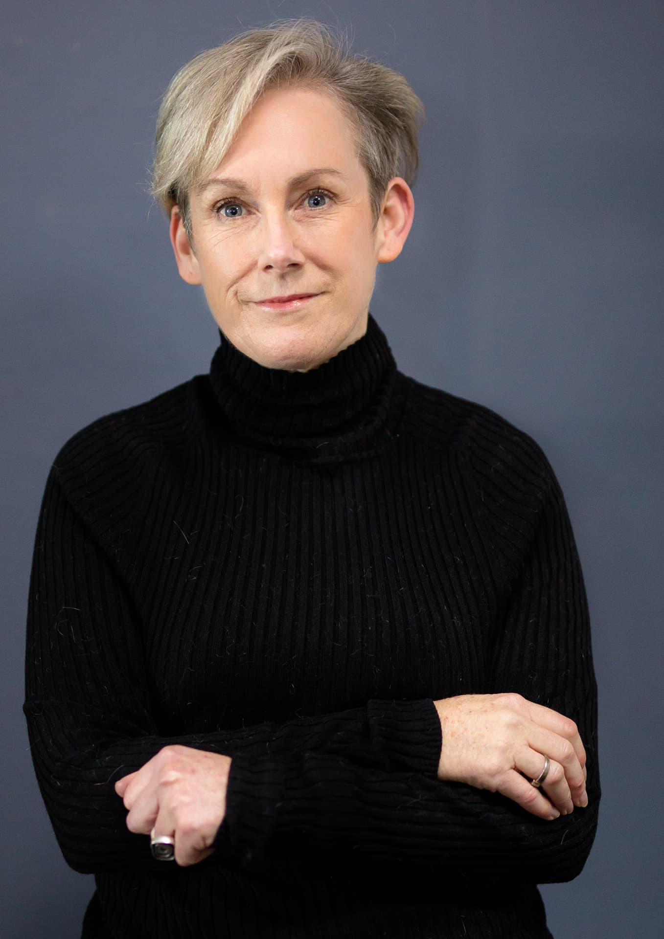 Robyn Leary, Copy Editor, with short blonde hair in a black turtleneck with arms folded